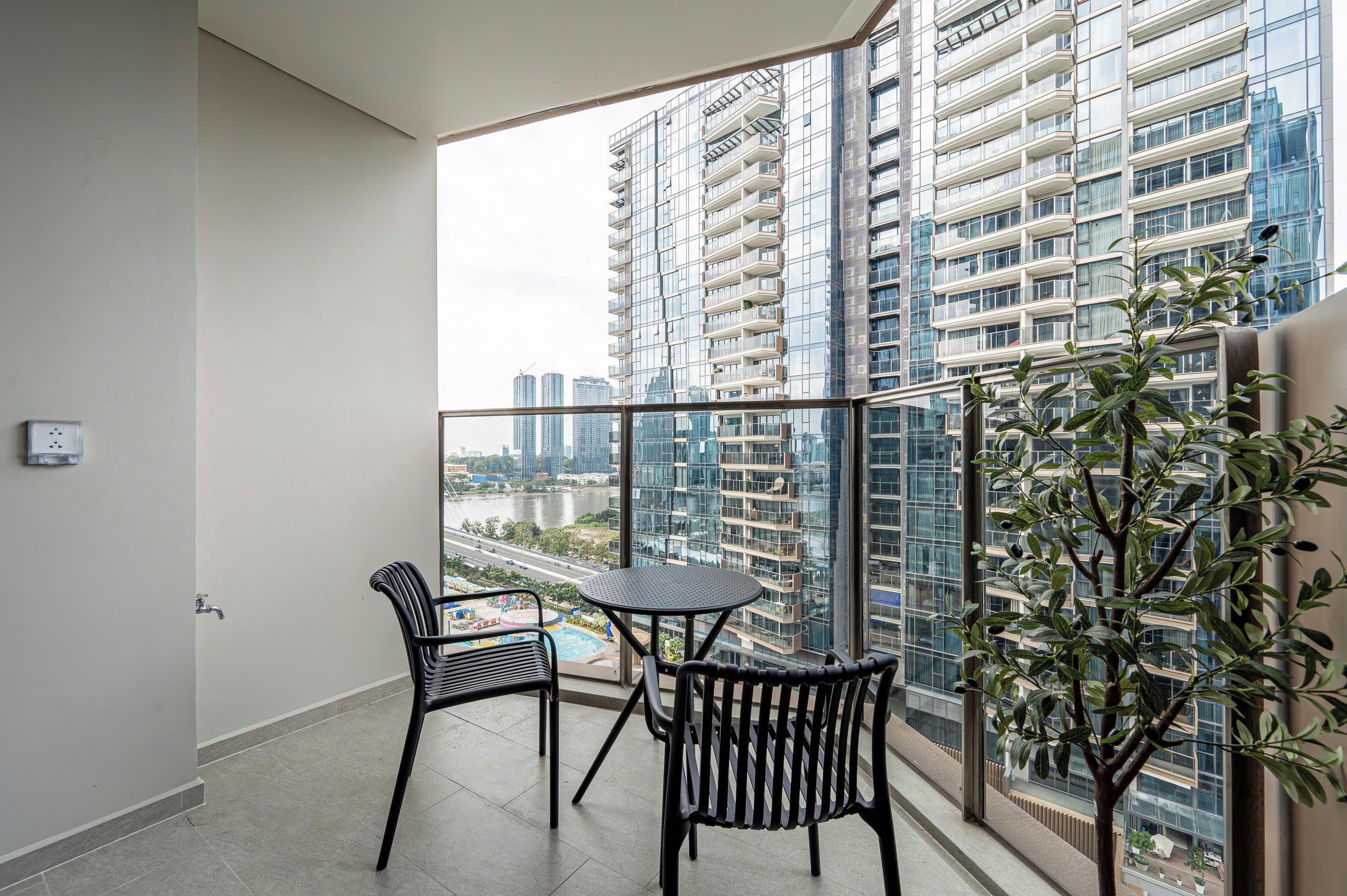 A balcony with a table and chairs, a potted plant, and a view of high-rise buildings.