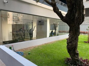 A modern building with a glass facade, a tree in the foreground, and a grassy area with a hose. - Brand-New Studio 150m from Vila Madalena Metro WSS144 (São Paulo)