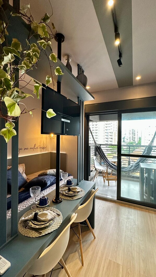 Ein modernes Wohnzimmer mit großem Fenster, einer Couch, einem Esstisch gedeckt mit Tellern und Gläsern, und einer Hängematte draußen.