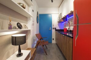 Une cuisine de taille réduite avec une porte bleue, un réfrigérateur rouge et une chaise en bois.