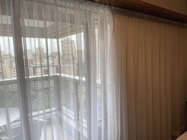 Ein Balkon mit transparenten Vorhängen, einem weißen Stuhl und Blick auf Gebäude.
