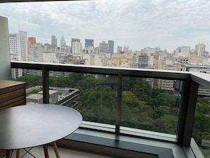 Un balcó amb taula i cadires, vista a un paisatge urbà amb edificis i vegetació.