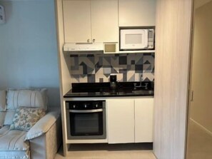 A compact kitchen with a microwave, oven, and a patterned backsplash. - 1BR Apt w/ Pool, Parking & Metro – Campo Belo EGB124 (São Paulo)