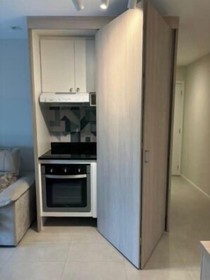 A compact kitchen with a built-in oven and cabinets, a small dining area with a table and chairs, and a sliding door leading to another room. - 1BR Apt w/ Pool, Parking & Metro – Campo Belo EGB124 (São Paulo)