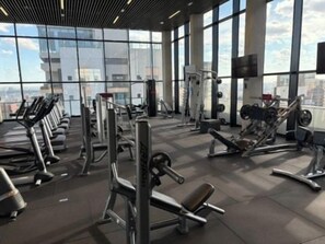 Ein Fitnessstudio mit verschiedenen Trainingsgeräten, großen Fenstern und Blick auf die Stadt.