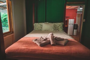 A room with a bed, a green wall, a window, and a kitchenette.
