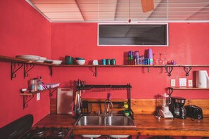 A kitchen with a red wall, wooden shelves, a sink, and various kitchen appliances.