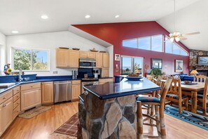 A modern kitchen with a stone island, wooden cabinets, and a dining area with a blue table and wooden chairs. - Sweet Home Colorado!!!! Where the skies are Crystal Blue!!!! (Kremmling)