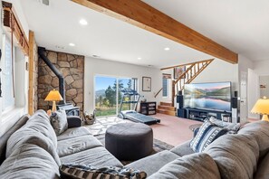 A spacious living room with a stone wall, a treadmill, a large flat-screen TV, and a staircase leading to an upper level. - Sweet Home Colorado!!!! Where the skies are Crystal Blue!!!! (Kremmling)