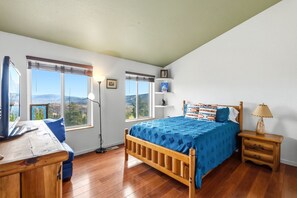 Een slaapkamer met een houten bed, een bureau, een lamp en uitzicht op het omliggende landschap.