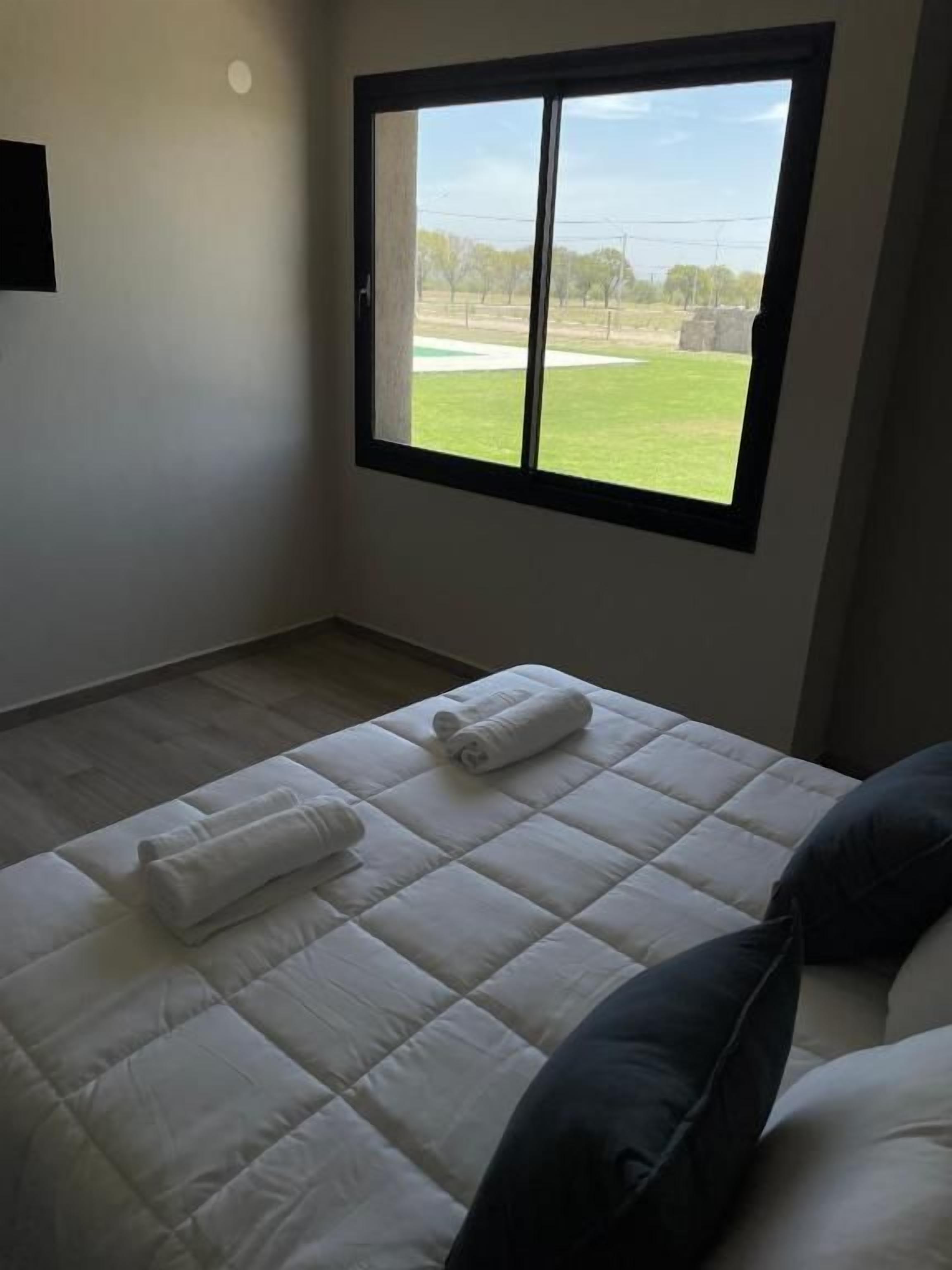 Una camera da letto con un'ampia finestra, un letto con biancheria bianca e vista su un campo verde.