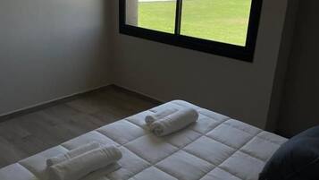 Una camera da letto con un'ampia finestra, un letto con biancheria bianca e vista su un campo verde.