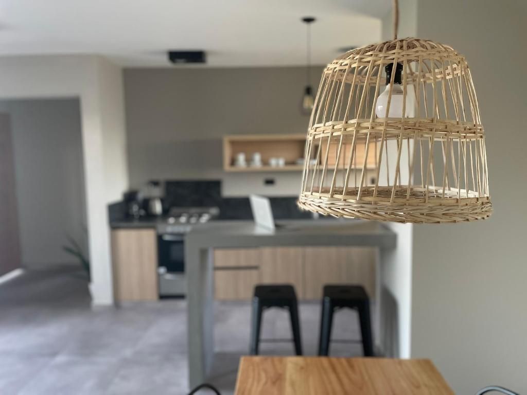 A modern kitchen with a central island, black bar stools, and a hanging woven light fixture.