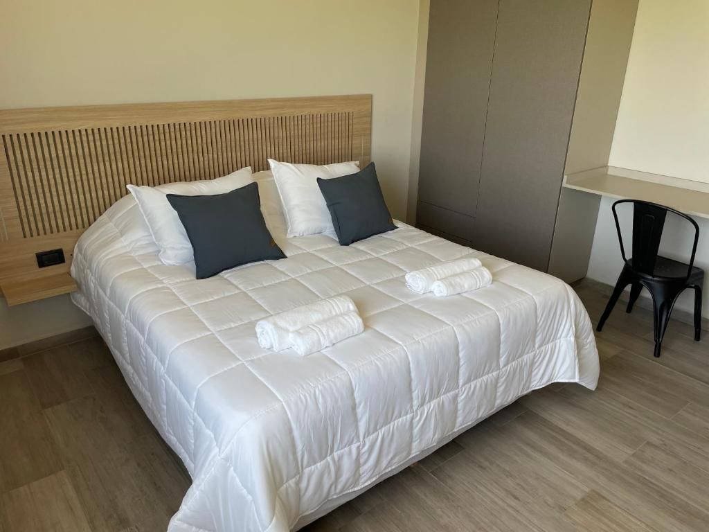 A neatly made bed with a white duvet and two pillows, a wooden headboard, and a small table with a chair beside it.