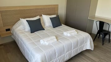 A neatly made bed with a white duvet and two pillows, a wooden headboard, and a small table with a chair beside it.