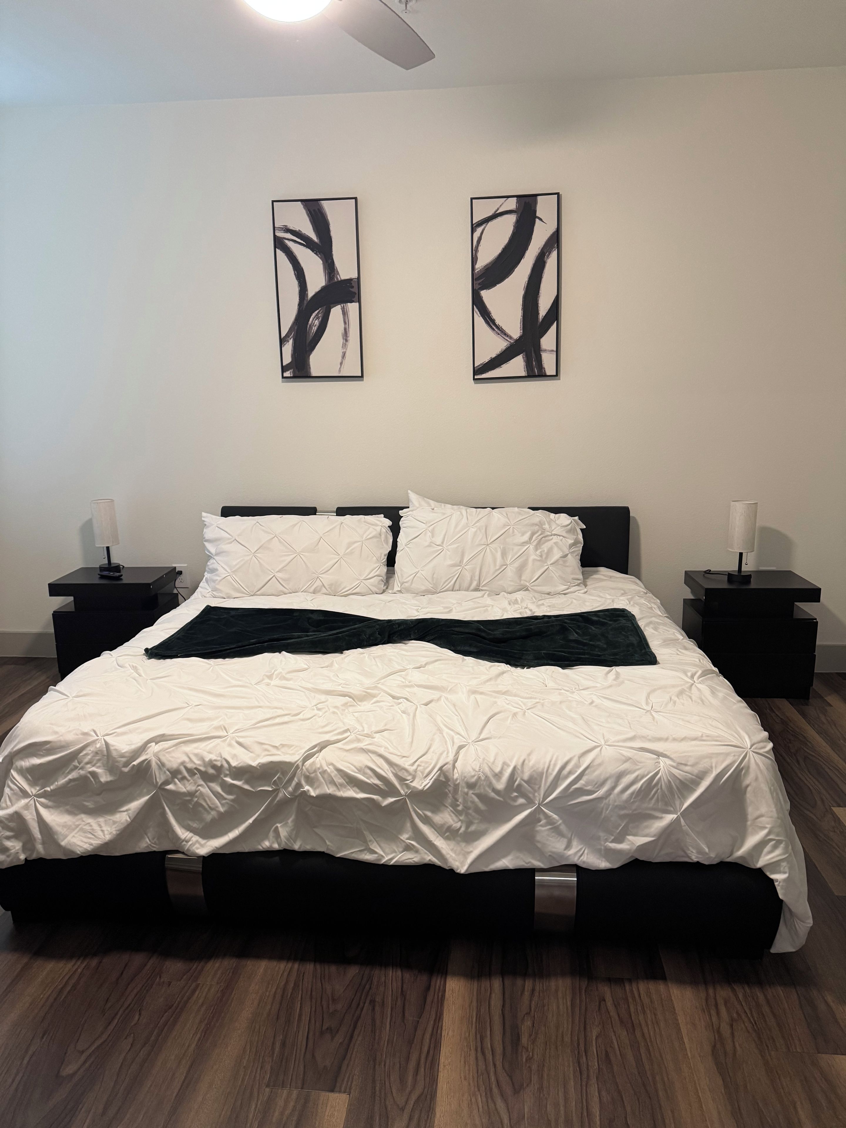 A bedroom with a bed, two nightstands, a ceiling fan, and abstract wall art.
