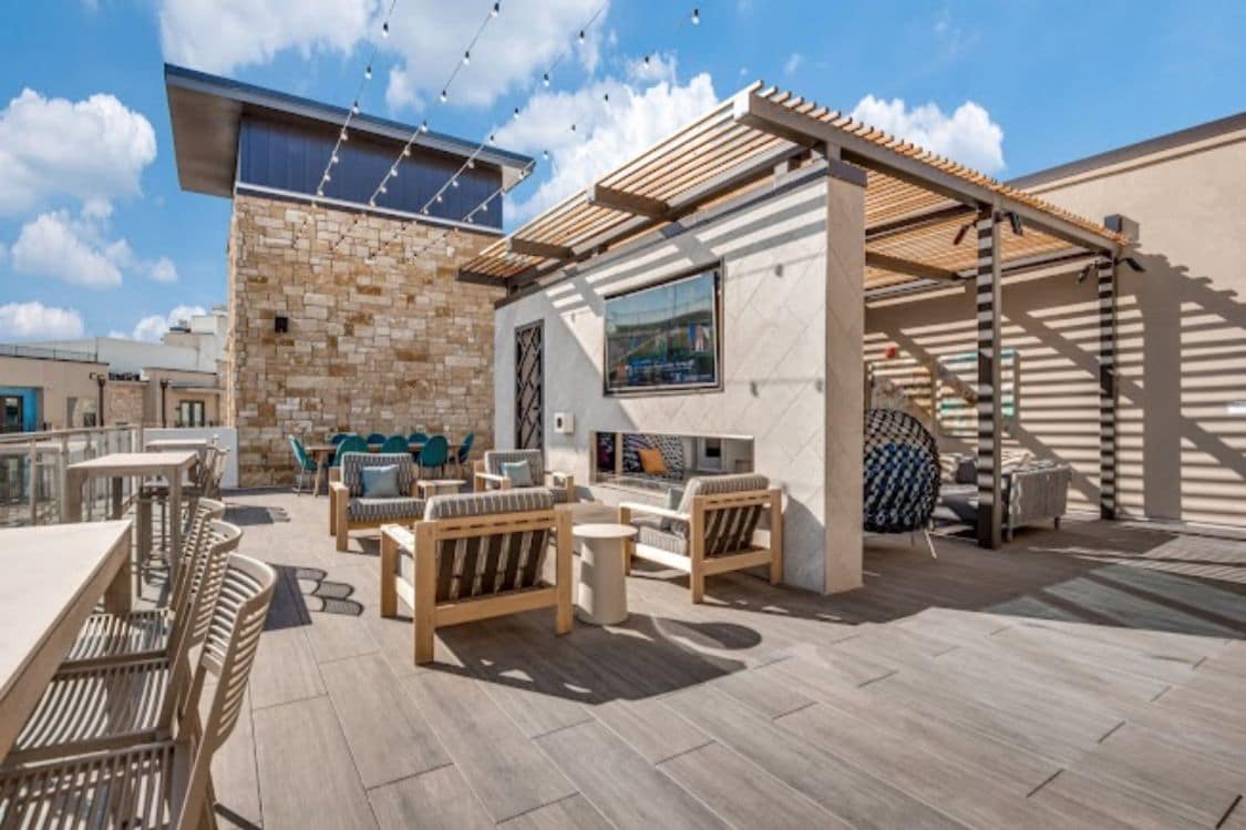 An outdoor patio with wooden furniture, a stone wall, and a pergola.