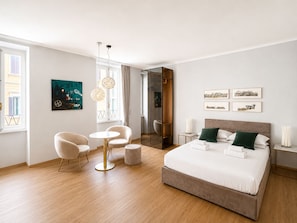 A modern hotel room with a large bed, a seating area with chairs, a small table, and artwork on the walls. - New! Marvellous Penthouse on Piazza Rondanini (Roma)
