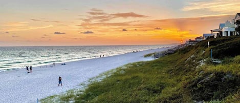 A beach with a sunset, grassy areas, and a building on the right.