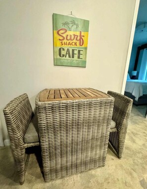 Ein Korbmöbel-Set aus Tisch und Stühlen vor einer Wand mit einem Schild, auf dem 'Surf Shack Cafe Open All Night' steht.