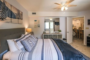 A bedroom with a bed, a ceiling fan, a dresser, and a dining area visible through an open door. - Stylish Top-Floor Ski-In/Out | Okemo Base Lodge (Ludlow)