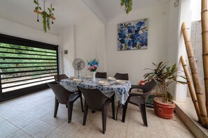 Un comedor con una mesa dispuesta para seis personas, rodeada de sillas, un ventilador y una planta en maceta.