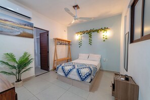 Un dormitorio con cama, ventilador de techo, luz empotrada en la pared, escalera de madera, planta en maceta y pared con planta colgante.