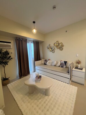A modern living room with a sofa, a coffee table, a side table with a book, and a decorative wall piece. - Cozy 1-bedroom condo in Serin East Tagaytay (Tagaytay City)