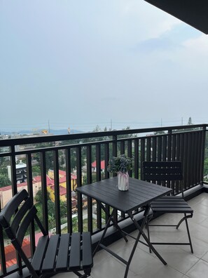 A balcony with a table and chairs, a vase with flowers, and a view of buildings and a body of water. - Cozy 1-bedroom condo in Serin East Tagaytay (Tagaytay City)