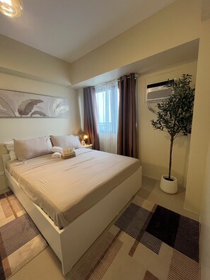 Ein Hotelzimmer mit Bett, Nachttisch, Lampe, einem Blumentopf und einer Wand-Klimaanlage.
