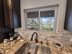 A kitchen with a double sink, a coffee maker, and a window with a view of trees and a fence. - Spacious 4 Bedroom Mountain Home Near Lake and Golf (Ruidoso)