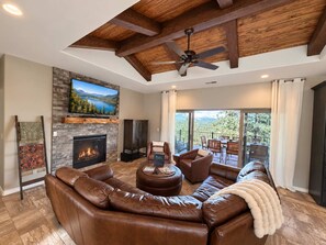 A spacious living room with a leather sectional sofa, a fireplace, a flat-screen TV mounted above it, and a balcony with outdoor seating. - Spacious 4 Bedroom Mountain Home Near Lake and Golf (Ruidoso)