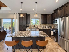A modern kitchen with dark wood cabinets, stainless steel appliances, and a large island with bar stools. - Spacious 4 Bedroom Mountain Home Near Lake and Golf (Ruidoso)