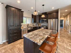 A modern kitchen with dark wood cabinets, stainless steel appliances, a granite island, and pendant lighting. - Spacious 4 Bedroom Mountain Home Near Lake and Golf (Ruidoso)