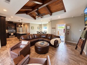 A spacious living area with a large L-shaped sectional sofa, a round ottoman, and a ceiling fan. - Spacious 4 Bedroom Mountain Home Near Lake and Golf (Ruidoso)
