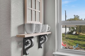Uno scaffale bianco con una finestra sopra, su cui sono posate diverse tazze e piattini bianchi.