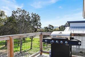 Una griglia barbecue su un balcone con vista su una zona verde e alberi.