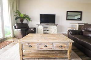 A living room with a wooden coffee table, leather sofas, a television, and a potted plant. - Emerald Escape - 3BR - Resort Pools & Bay Views (Panama City Beach)