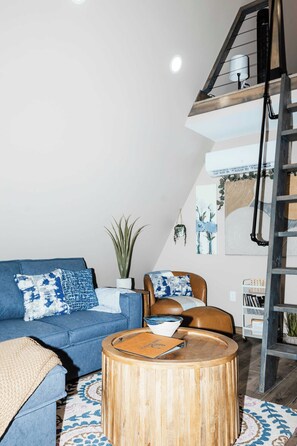 A modern living room with a blue sofa, a round wooden coffee table, and a brown leather chair. - Starlight - Pondside  Hot Tub - Game Room & Kayaks (Campton)