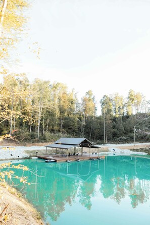 A tranquil outdoor swimming pool with a wooden deck and a covered seating area, surrounded by trees. - Starlight - Pondside  Hot Tub - Game Room & Kayaks (Campton)