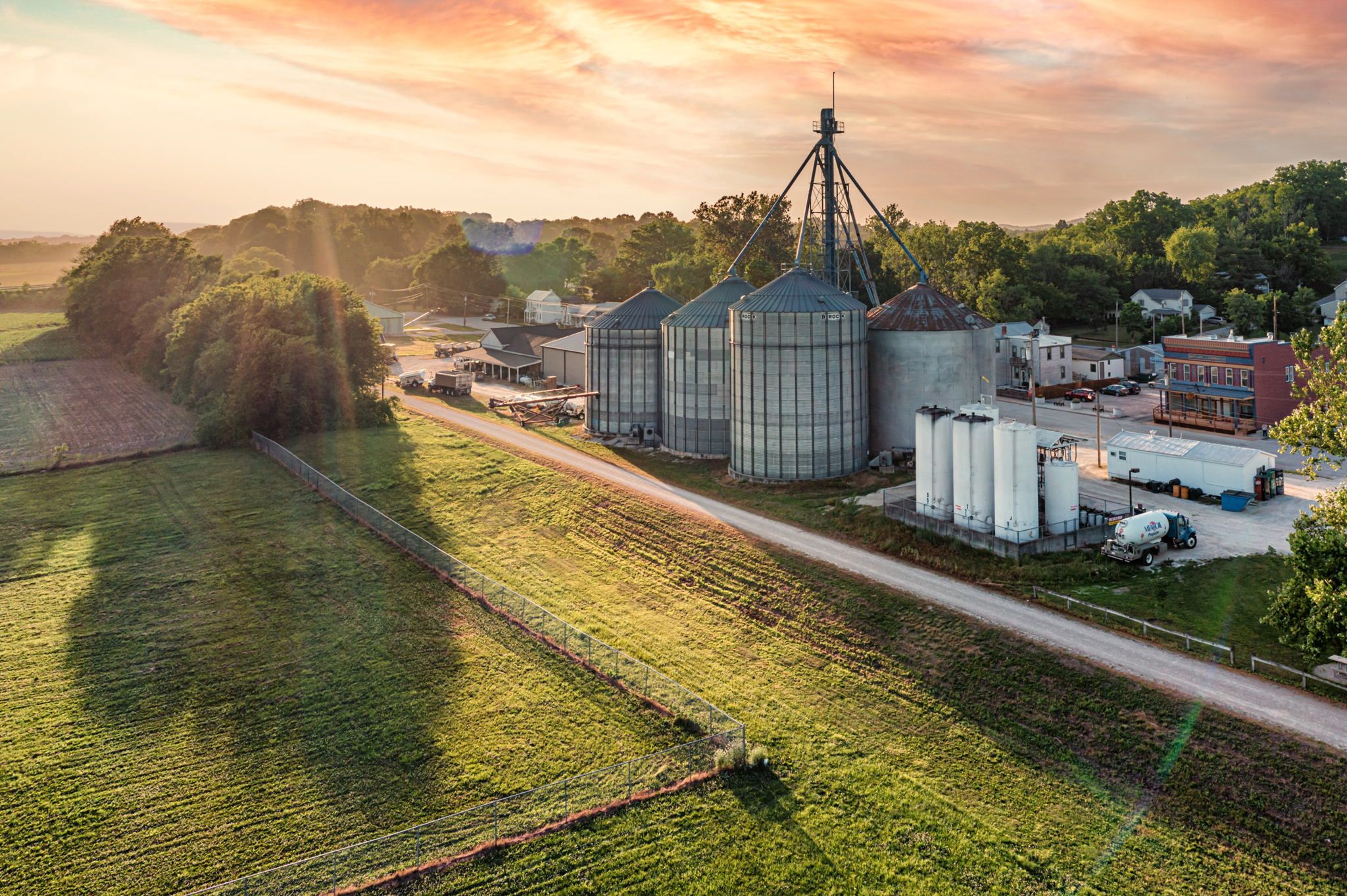 A rural landscape with grain silos, a road, and a small town with buildings.