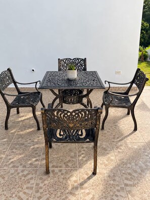 Een terras buiten met een vierkante tafel en vier stoelen, een plant in een pot op de tafel en een betegelde vloer.