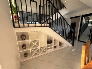 A staircase with a white wall and black railing, leading to a landing with shelves containing decorative items. - BellaHills by Ambar (San Juan)