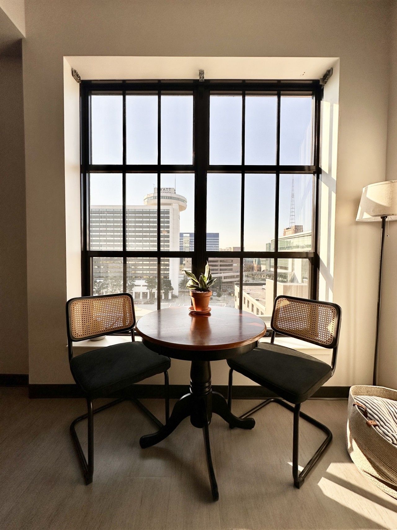 Una habitación con un ventanal grande, dos sillas, una mesita y una planta en maceta.
