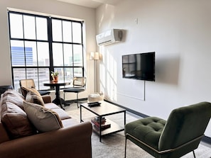 A modern living room with a sofa, armchair, coffee table, and a flat-screen TV mounted on the wall. - Deer District Studio Apt - One Block from Fiserv and Baird (Milwaukee)