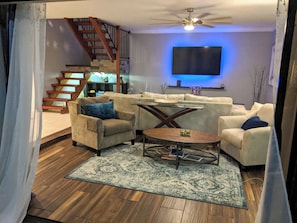 Un salon comprenant un ensemble de canapés, une table basse, un téléviseur fixé au mur et un escalier.