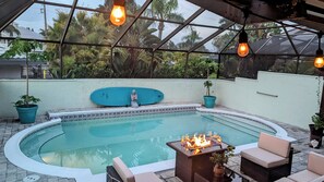 Une piscine agrémentée d’un foyer, entourée de sièges et de plantes en pot.