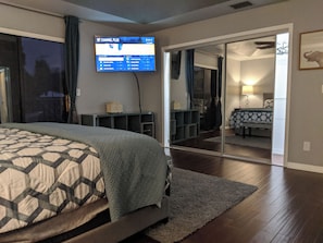A bedroom with a bed, a television mounted on the wall, a mirror, and a sliding door leading to a bathroom. - Private pool screened in—minutes from Bonita Beach. 2 Master Beds / 2.5 Baths. (Bonita Springs)