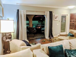 Un salon comprenant un canapé, une table basse et une lampe. Une porte vitrée donne accès à un espace extérieur aménagé avec un foyer et des chaises.