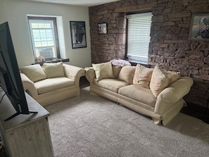 Una sala de estar con dos sofás beige, un televisor y decoración de pared de piedra.